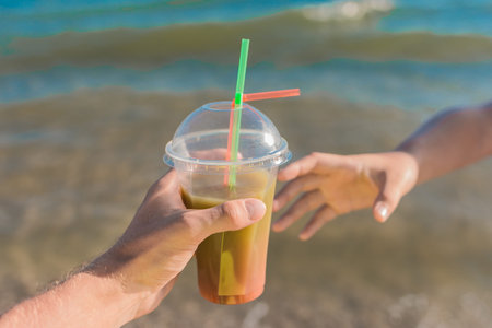 The guy's hand passes a colored chilled non-alcoholic cocktail into the girl's hand against the...