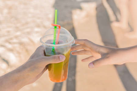 The guy's hand passes a colored chilled non-alcoholic cocktail into the girl's hand against the background of sea beach.の写真素材