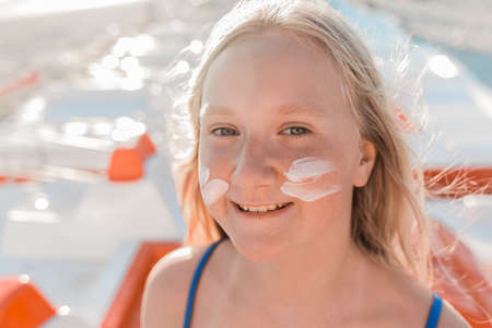 Close-up portrait of the face of a young positive attractive girl with sunscreen and sun protection on her cheeks.の写真素材