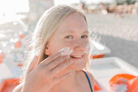 Close-up portrait of a young sweet and happy teenage girl smearing sunscreen on her face.の写真素材