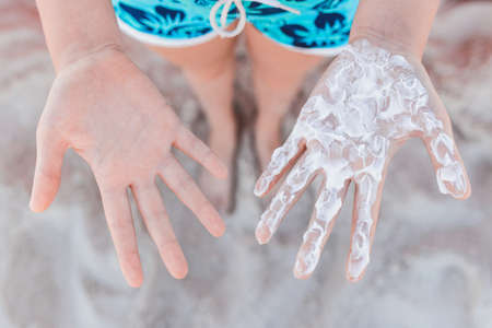 Hands of a young girl palms with sun cream and sun protection against the background of the beach.の写真素材