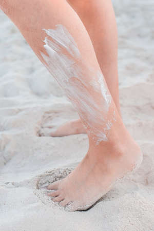 The legs of a young girl stand on the beach white sand with sunscreen on the skin.の写真素材