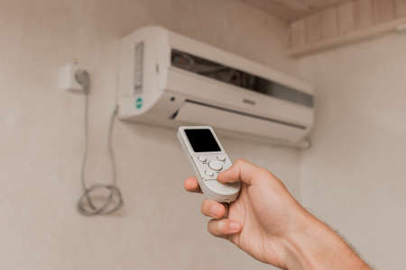 The guy's hand holds the remote control of the air conditioner. Cooling and temperature control in the room of the house.の写真素材