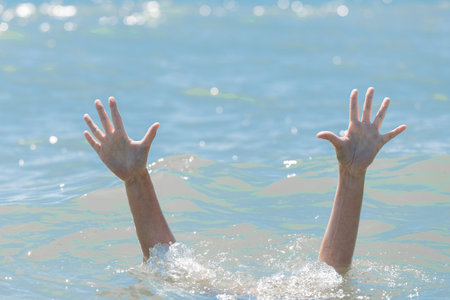 A hands from under the water of a drowning girl, help and urgent rescue of a person during a dangerous swimming, sos.の写真素材