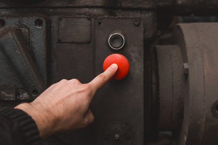 The worker's hand presses the red button on the old system of industrial equipment with his finger.の写真素材