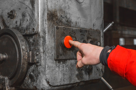 The hand of a man in a work suit presses his finger on the red button to control old industrial...