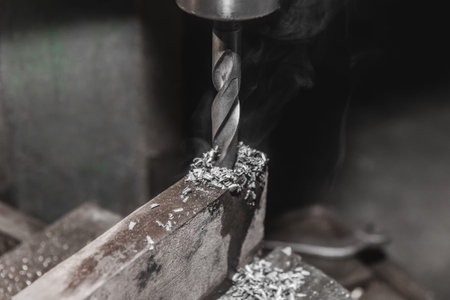 Thick drill drilling old iron bar, steel work equipment close-up.