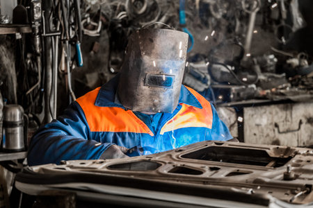 The welder in the protective shield is engaged in welding works and repair of the automobile door in...