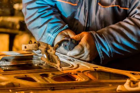 The hands of a male industrial welder worker hold a welding machine, and are engaged in welding on...