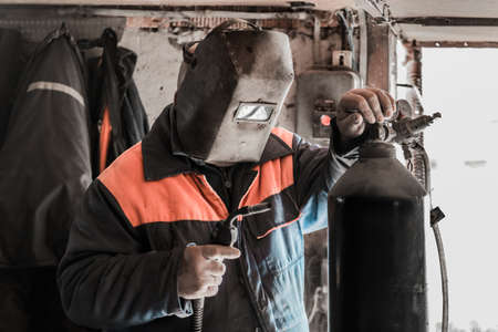 A man welder worker stands in front of a welding machine and a carbon dioxide cylinder, with a gearbox in the shop of an industrial plant.の写真素材