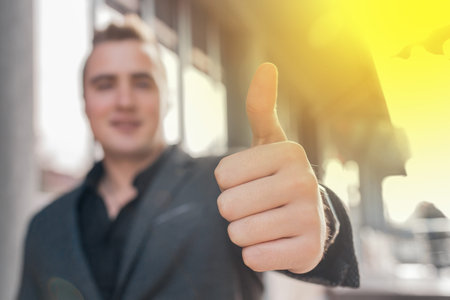 A young man shows a close-up of a thumbs up class against a street outdoor background.の写真素材