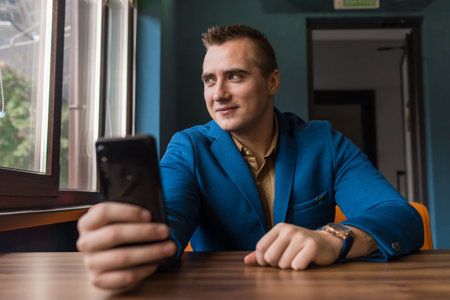 A positive, smiling young guy of European appearance, a stylish businessman, looks at a window and...