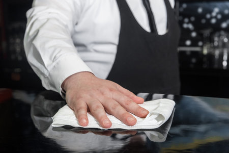 The hand of a professional bartender wipes the bar counter with a napkin or cloth, cleans and...