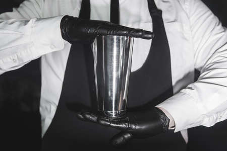 Hands of a professional bartender in latex rubber gloves hold a tool for preparing and mixing alcoholic cocktail shaker, close-up.の写真素材