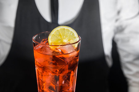 Red alcoholic cocktail chilled drink in glass decorated with a slice of sliced lemon, close-up.