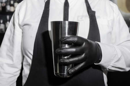 The hand of a professional bartender man in black latex glove holds a tool for mixing and making shaker cocktails.の写真素材