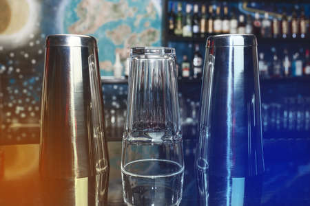 2 shakers of bar instruments for mixing and preparing alcoholic cocktails and drinks with a glass on the bar counter.の写真素材
