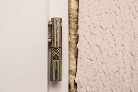 Old door steel hinge, repair and fixation of the wall with construction polyurethane mounting foam, close-up.の写真素材
