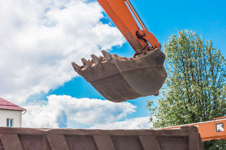 Excavation works. The bucket of the tractor loads the soil with a shovel into the back of a dump truck on the construction site.の写真素材