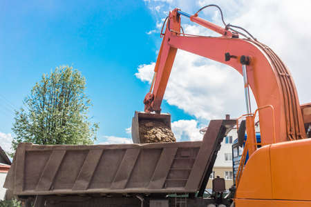 Excavation works. The bucket of the tractor loads the soil with a shovel into the back of a dump truck on the construction site.の写真素材