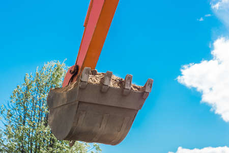 Excavation works. Tractor bucket digging the ground on a construction site against the sky.の写真素材