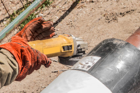The hands of an industrial worker in working mittens use an electric-grinding equipment tool on a...