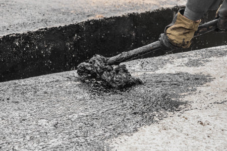 A construction worker is engaged in dirty manual work to repair and apply black bitumen...