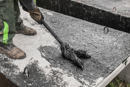 A construction worker is engaged in dirty manual work to repair and apply black bitumen...