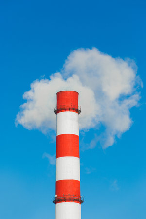 Pollution of the environment, ecology and air. Withdrawal of combustion products of soot, smoke and gases from the pipe of an industrial plant into the atmosphere against the background of a blue sky.の写真素材