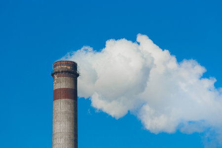 Pollution of the environment, ecology and air. Withdrawal of combustion products of soot, smoke and gases from the pipe of an industrial plant into the atmosphere against the background of a blue sky.の写真素材