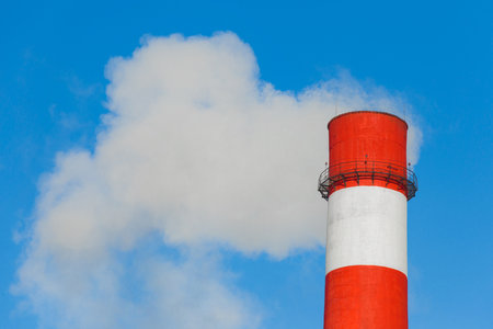 Pollution of the environment, ecology and air. Withdrawal of combustion products of soot, smoke and gases from the pipe of an industrial plant into the atmosphere against the background of a blue sky.の写真素材