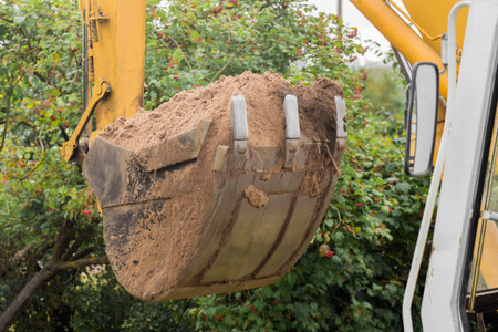 A bucket of excavator with a pile of land close-up. Excavation work in the industrial zone.