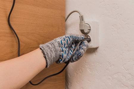 The hand of a male construction worker in protective gloves connects a plug to a double socket against the background of a wall.の写真素材
