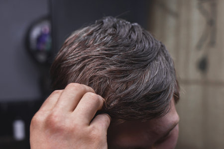 A man's hand touches his dark long hair necessary for a haircut and in need of hairdressing services.の写真素材
