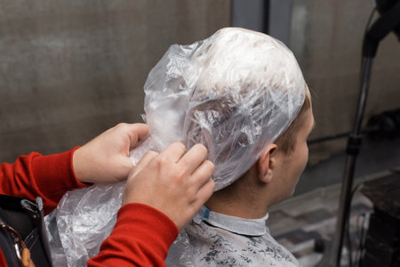 Barber's hands, close-up, remove a protective film from the client's head, the process of dyeing hair in a hairdresser.の写真素材
