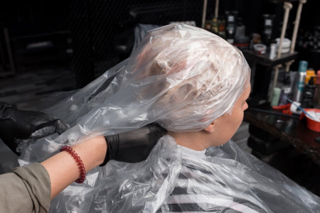The hands of a professional hairdresser fix a plastic film on the client's head before dyeing her hair in a salon or barbershop.の写真素材