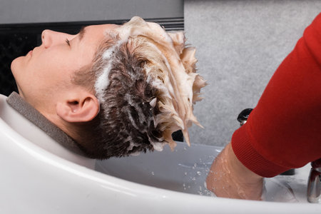The client is a young European guy in the process of washing his hair in a barbershop before cutting his hair.の写真素材