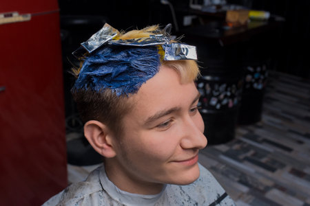 Handsome smiling young guy portrait European in the process of dyeing hair in color in a barbershop.の写真素材