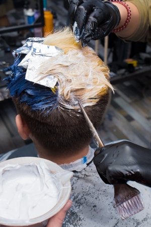 The hands of a professional barber hold a brush for men's hair coloring next to white dye in a barbershop at work.の写真素材