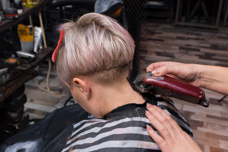 The hands of a girl, a professional barbershop worker, make a woman's hair cut for an adult woman, a client of a hairdresser.の写真素材