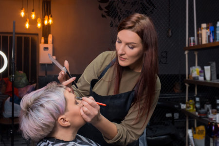 Cute attractive brunette girl professional barbershop European makes, make-up a palette of shadows...