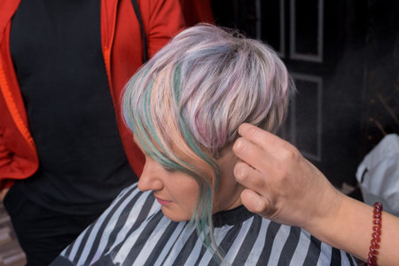 The hand of a hairdresser girl in a salon works with the hairstyle of a client of an adult woman...
