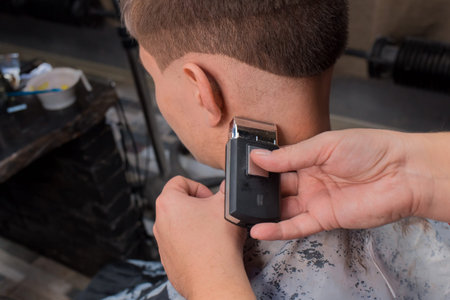 The barber's hands cut the back of the head of the client's young guy with a special razor for a...