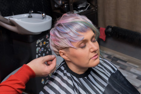 The hands of an experienced barber men straighten the hairstyle of an adult woman, a client of a barbershop with a stylish fashionable bob hairstyle, creative color hair coloring.の写真素材