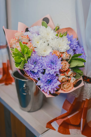 A bouquet of flowers, purple and white chrysanthemums and cream-colored roses stand in a metal bucket in the water against the background of the interior.の写真素材