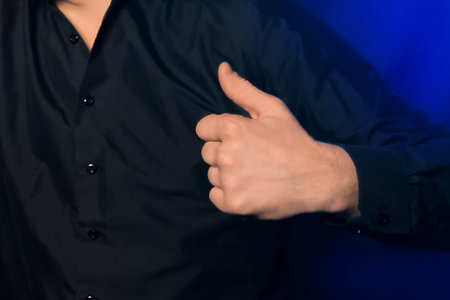 Person hand shows class cool thumb top close-up on dark background.の写真素材