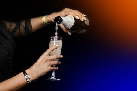 The girl's hands are engaged in self-service, pouring herself champagne from a bottle into a glass on a black background.の写真素材