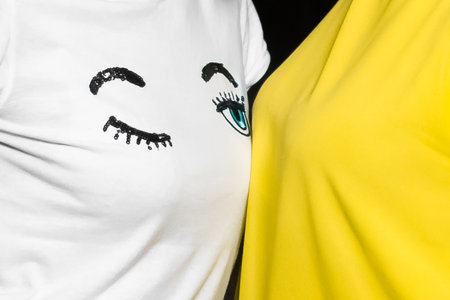 White cute T-shirt with a pattern of a winking blue eye print drawing on light yellow background.の写真素材