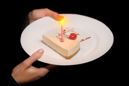 Person's hands holding a plate, a surprise with a white sweet dessert, a cheesecake with a candle...