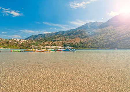 paddle boat rental at Kournas lake on sunny summer day with bright ripples on water and sun shining above mountains, Crete, Greeceの写真素材
